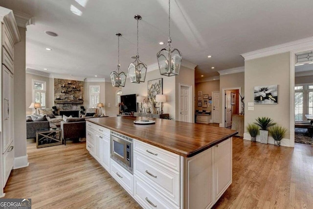 kitchen with light hardwood / wood-style floors, stainless steel microwave, wood counters, a center island, and white cabinetry