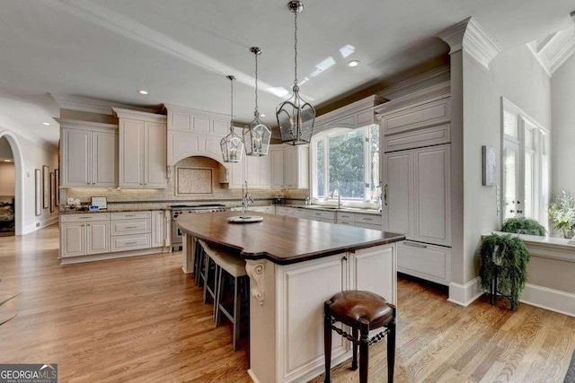 kitchen featuring decorative light fixtures, a kitchen island with sink, light wood-type flooring, and a kitchen bar