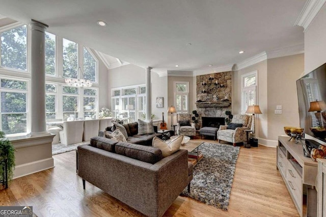 living room with a high ceiling, light wood-type flooring, decorative columns, a stone fireplace, and ornamental molding