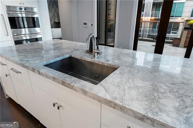 kitchen featuring stainless steel oven, white cabinets, and light stone counters