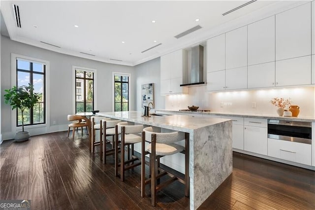 kitchen featuring a center island with sink, wall chimney range hood, white cabinets, and dark hardwood / wood-style flooring