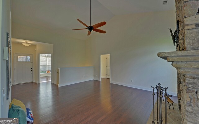 unfurnished living room with ceiling fan, a stone fireplace, dark wood-type flooring, and high vaulted ceiling