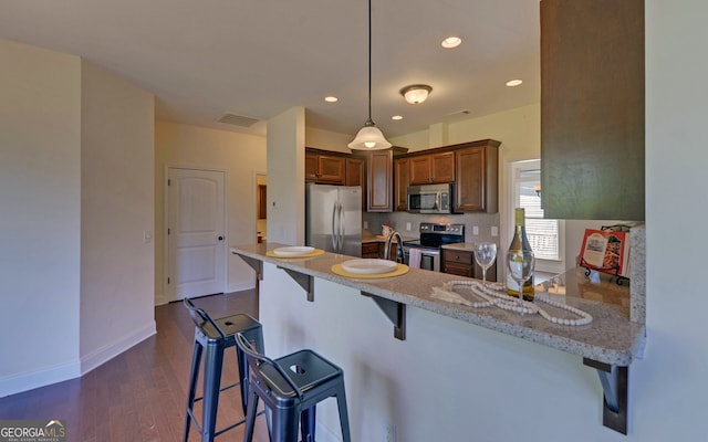 kitchen featuring a kitchen bar, decorative light fixtures, stainless steel appliances, and kitchen peninsula