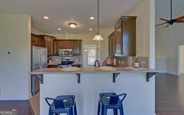 kitchen with a kitchen bar, appliances with stainless steel finishes, kitchen peninsula, dark wood-type flooring, and decorative light fixtures