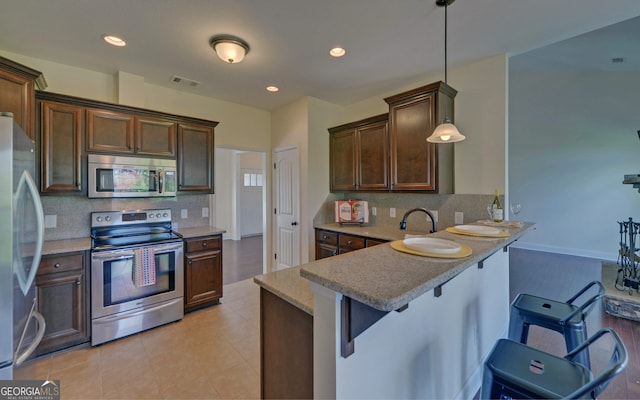 kitchen with stainless steel appliances, a kitchen breakfast bar, kitchen peninsula, pendant lighting, and decorative backsplash