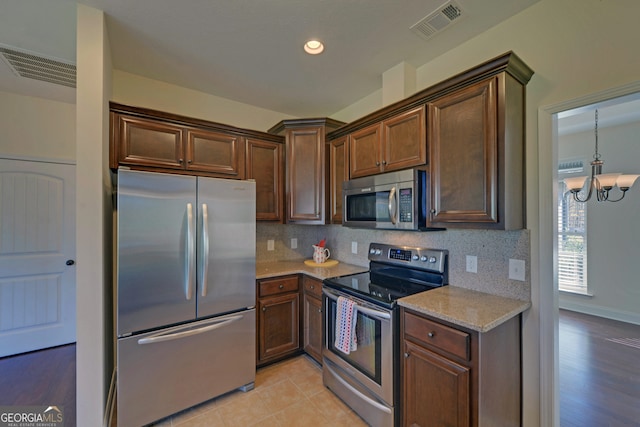 kitchen with stainless steel appliances, an inviting chandelier, light stone counters, light hardwood / wood-style flooring, and backsplash