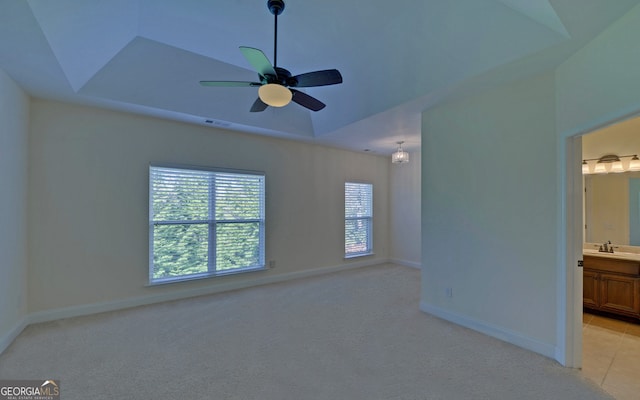 empty room with light colored carpet, ceiling fan, a tray ceiling, and sink