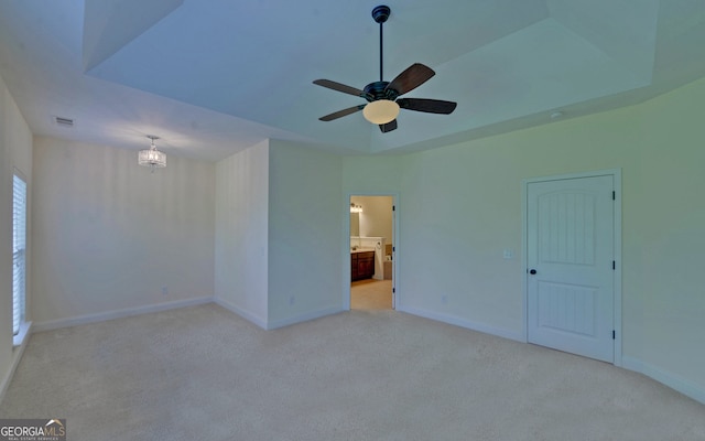 carpeted empty room featuring ceiling fan with notable chandelier and a raised ceiling