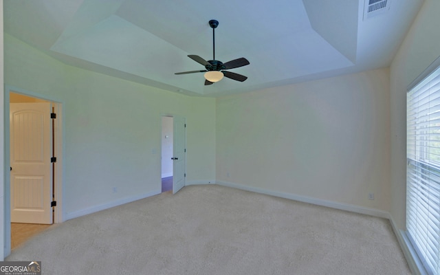 carpeted empty room with a raised ceiling and ceiling fan