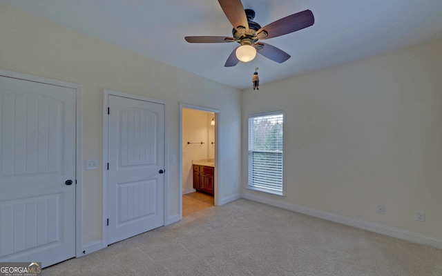 unfurnished bedroom featuring connected bathroom, ceiling fan, light carpet, and two closets