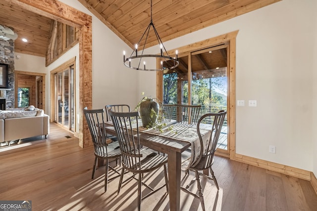 dining space with wood ceiling, a stone fireplace, hardwood / wood-style floors, vaulted ceiling, and a notable chandelier