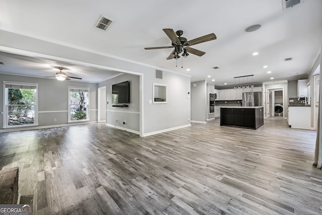 unfurnished living room featuring washer / dryer, sink, hardwood / wood-style floors, ceiling fan, and ornamental molding