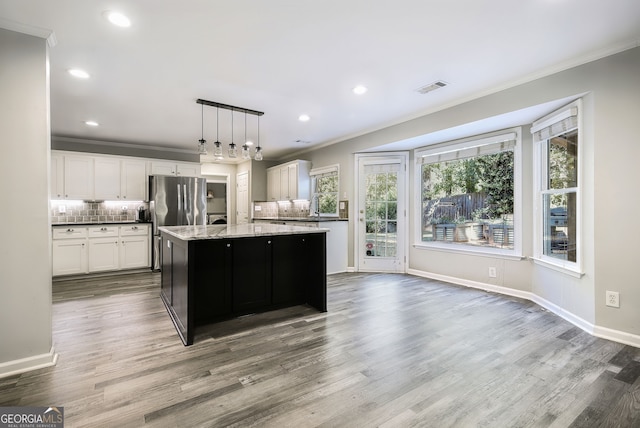 kitchen with decorative backsplash, hanging light fixtures, an island with sink, white cabinetry, and hardwood / wood-style flooring