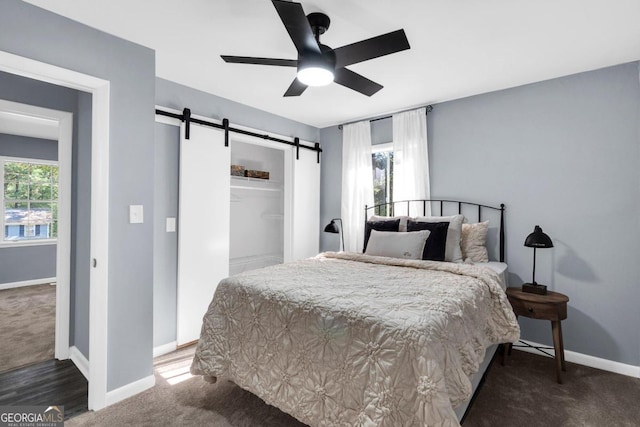 bedroom with multiple windows, a barn door, dark carpet, and ceiling fan