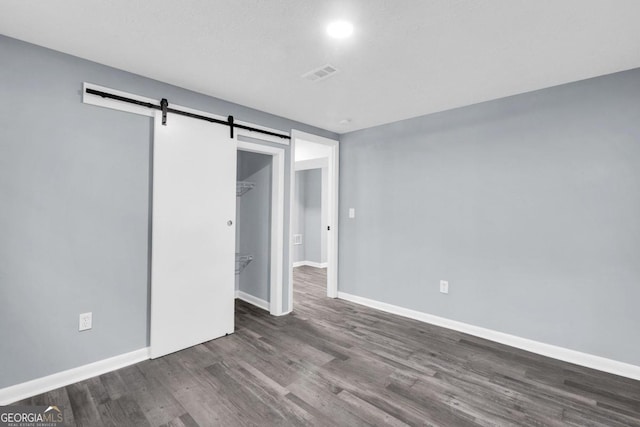 unfurnished bedroom with a closet, dark hardwood / wood-style floors, and a barn door