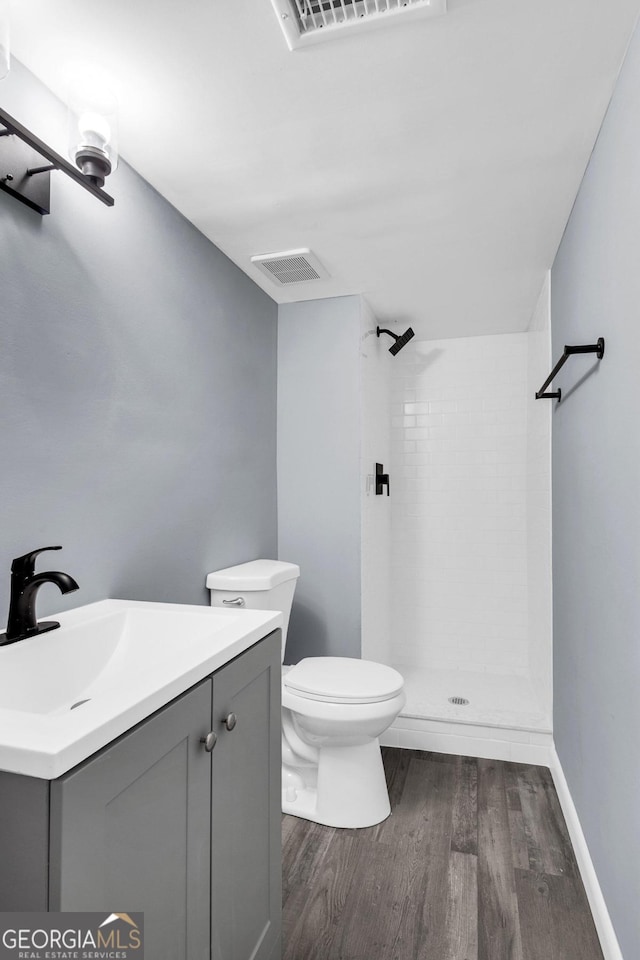 bathroom with a tile shower, hardwood / wood-style floors, toilet, and vanity