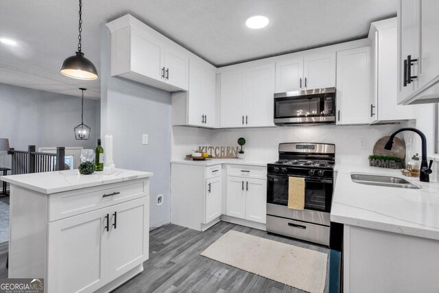 kitchen featuring sink, light wood-type flooring, stainless steel appliances, pendant lighting, and white cabinets