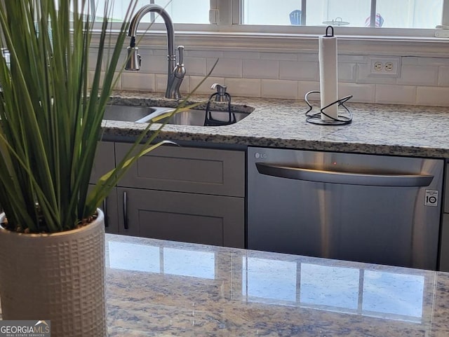 kitchen with stainless steel dishwasher, backsplash, light stone counters, and sink