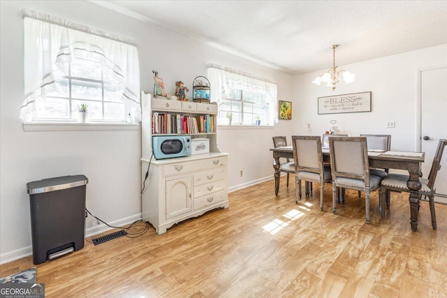 dining area with a textured ceiling, light hardwood / wood-style flooring, and a chandelier