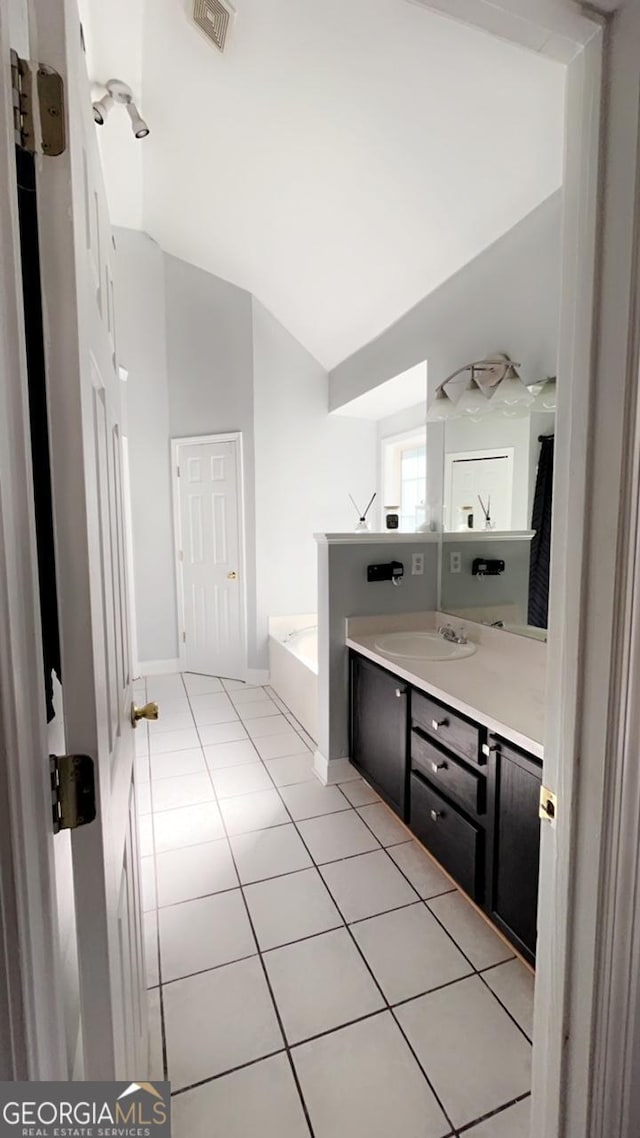 bathroom with tile patterned flooring, vanity, a tub to relax in, and lofted ceiling