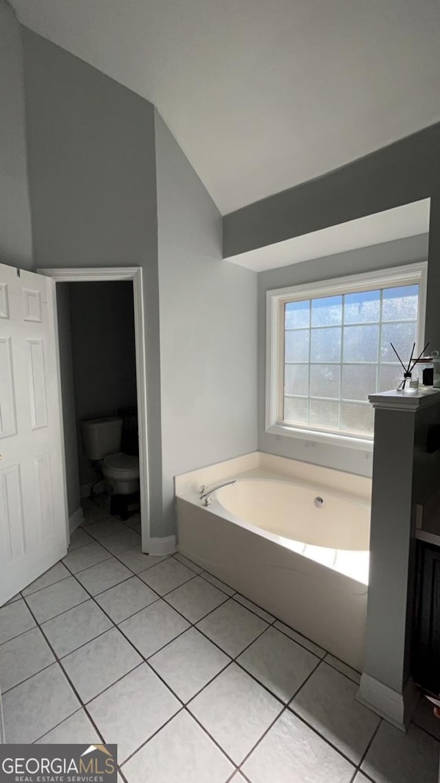 bathroom featuring tile patterned floors, toilet, lofted ceiling, and a tub to relax in