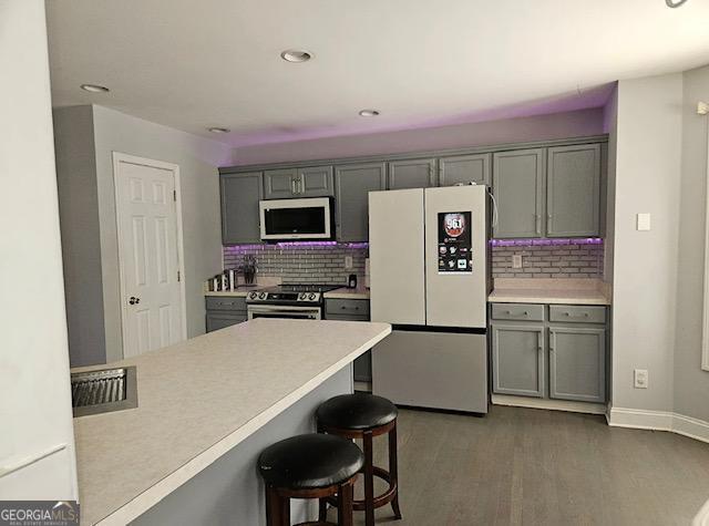 kitchen with a kitchen bar, decorative backsplash, gray cabinets, appliances with stainless steel finishes, and dark hardwood / wood-style flooring