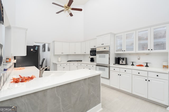 kitchen featuring black appliances, ceiling fan, white cabinets, sink, and a towering ceiling