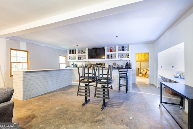 dining area featuring concrete floors, built in shelves, a wealth of natural light, and bar area