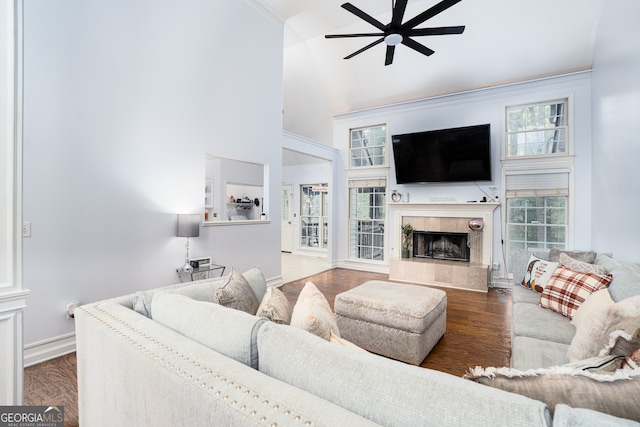 living room with ceiling fan, dark hardwood / wood-style flooring, crown molding, a towering ceiling, and a tile fireplace