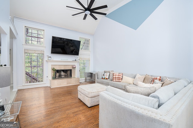 living room featuring ceiling fan, high vaulted ceiling, a tiled fireplace, and wood-type flooring