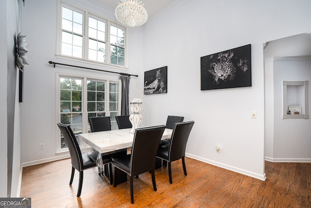 dining area featuring a towering ceiling, ornamental molding, a chandelier, and hardwood / wood-style flooring