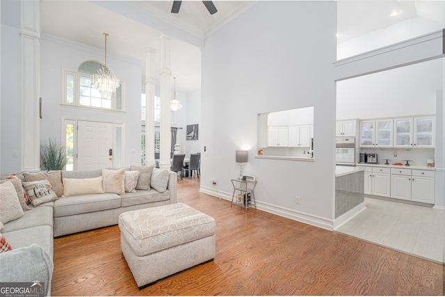 living room featuring ornamental molding, light wood-type flooring, a towering ceiling, and ceiling fan with notable chandelier