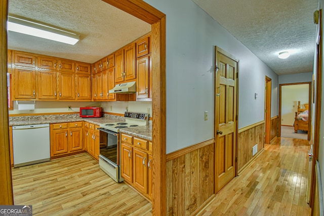 kitchen with white appliances, a textured ceiling, light hardwood / wood-style flooring, wooden walls, and light stone countertops