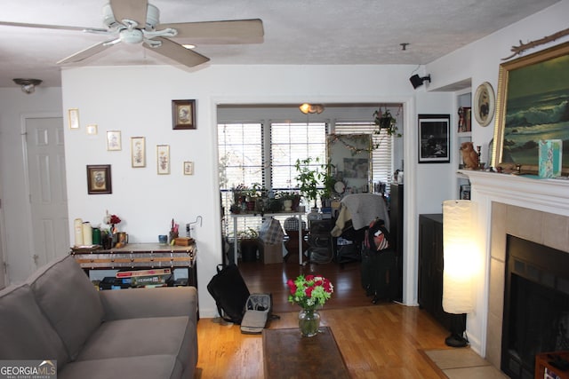 living room with a textured ceiling, a tiled fireplace, ceiling fan, and wood-type flooring