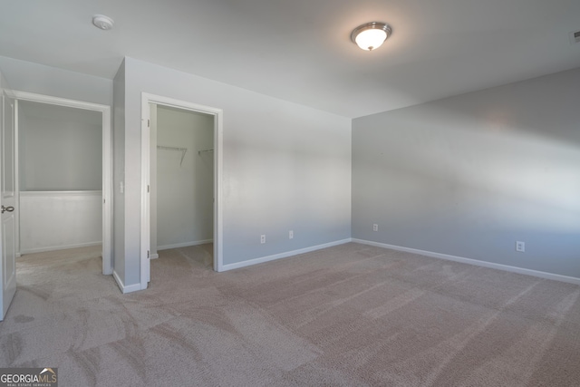 unfurnished bedroom with a walk in closet, light colored carpet, and a closet