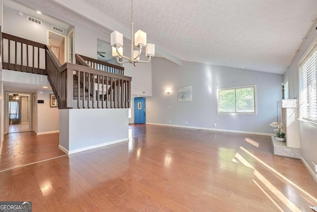 unfurnished living room with high vaulted ceiling, beamed ceiling, hardwood / wood-style floors, an inviting chandelier, and a textured ceiling