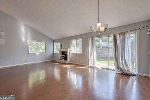 unfurnished living room with wood-type flooring, a notable chandelier, a textured ceiling, and a healthy amount of sunlight