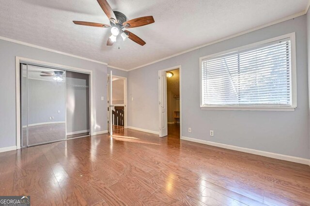 unfurnished bedroom with a closet, hardwood / wood-style flooring, ornamental molding, and ceiling fan