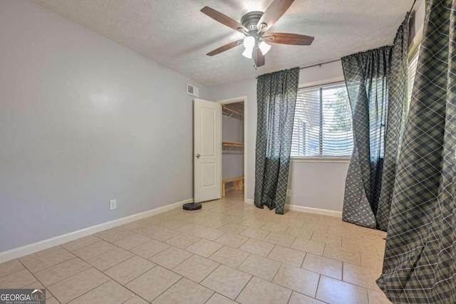 unfurnished bedroom with ceiling fan, light tile patterned flooring, a textured ceiling, a closet, and a spacious closet