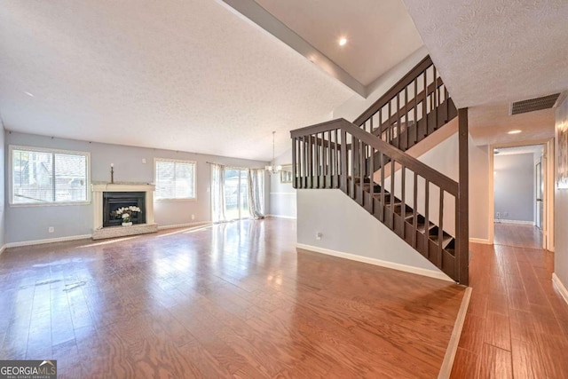 unfurnished living room with an inviting chandelier, a textured ceiling, and hardwood / wood-style flooring