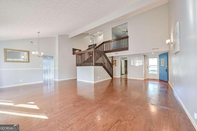 unfurnished living room with ceiling fan with notable chandelier, high vaulted ceiling, hardwood / wood-style flooring, and a textured ceiling