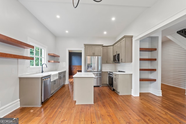 kitchen with gray cabinets, light wood-type flooring, tasteful backsplash, a kitchen island, and appliances with stainless steel finishes