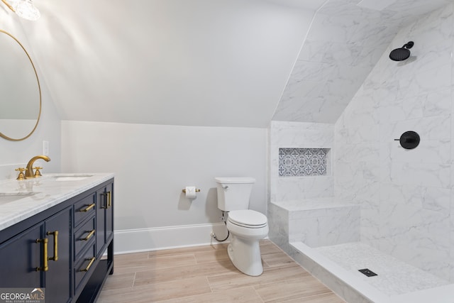 bathroom with vaulted ceiling, toilet, tiled shower, and vanity