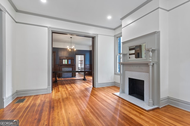 unfurnished living room with a notable chandelier, a tiled fireplace, light hardwood / wood-style floors, and crown molding