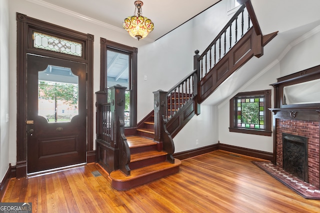 entryway featuring a brick fireplace, a healthy amount of sunlight, crown molding, and hardwood / wood-style floors