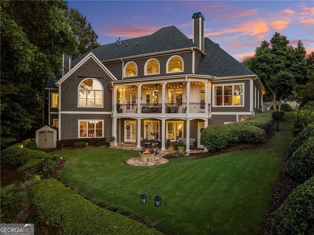 back house at dusk featuring a storage shed, a balcony, and a lawn