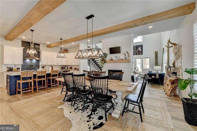 dining space featuring a fireplace, light hardwood / wood-style flooring, and beamed ceiling