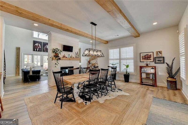 dining area with beamed ceiling, plenty of natural light, a large fireplace, and light hardwood / wood-style flooring