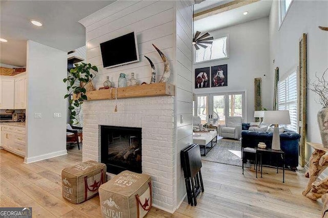 living room featuring a brick fireplace, light hardwood / wood-style flooring, and a high ceiling