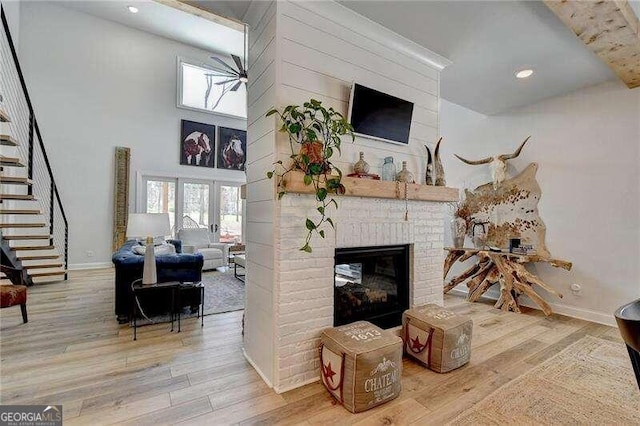 living room with wood-type flooring, a towering ceiling, and a brick fireplace